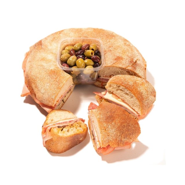 Sliced muffuletta ring sandwich with deli meats, cheese, and central olive salad, arranged on a serving tray.